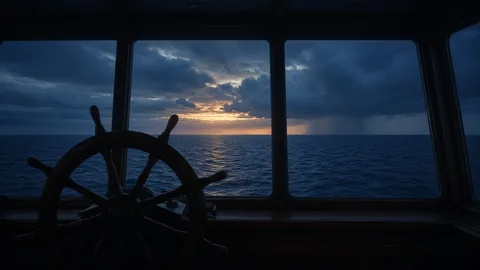 Ship's wheel on a dark bridge facing a navy sea at sunrise
